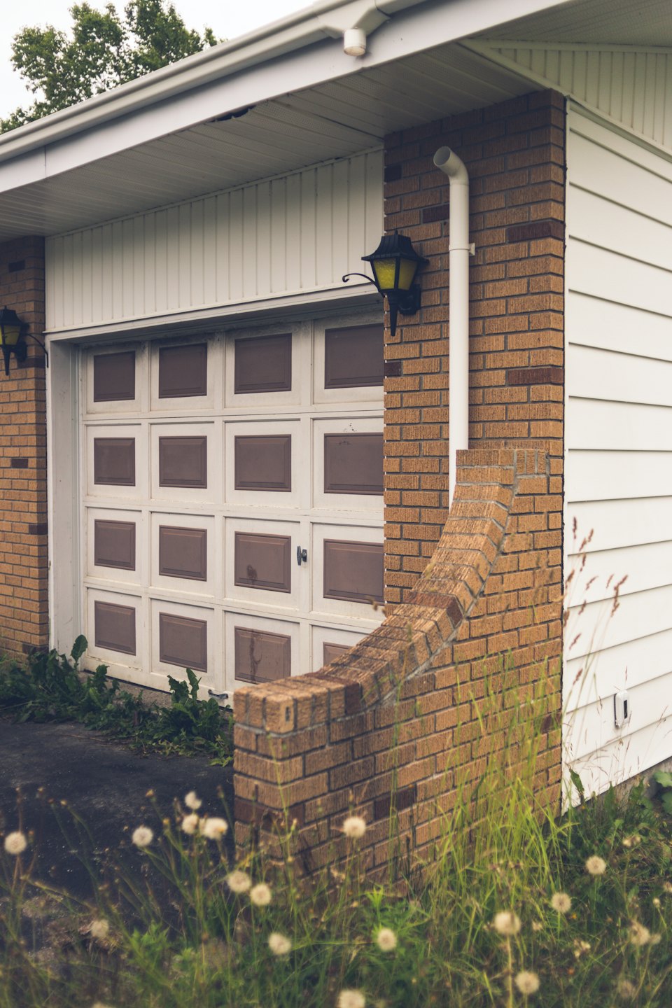 Weeds grow near a residential garage with white panel doors.