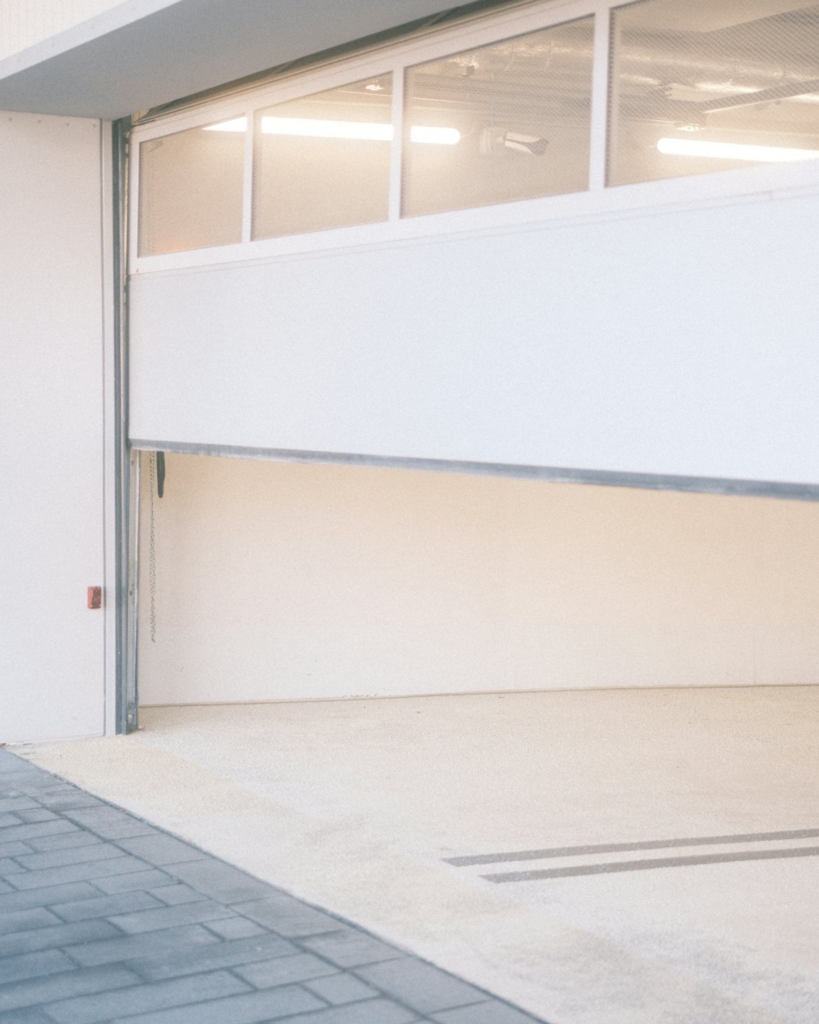Partially open modern white garage door revealing an empty interior.