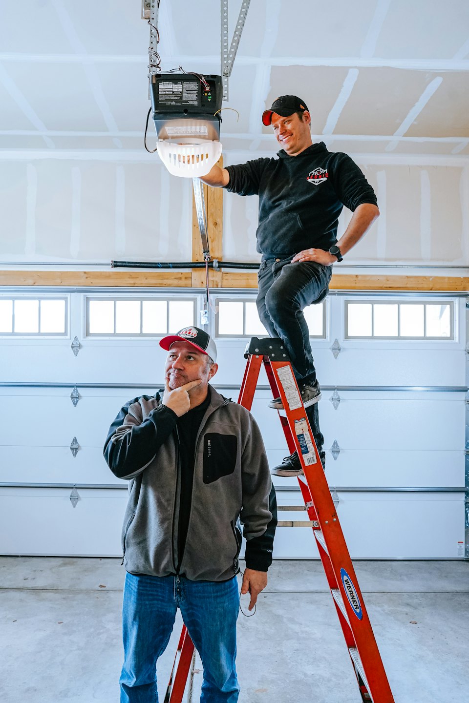 Men installing a garage door opener in a brightly lit garage.