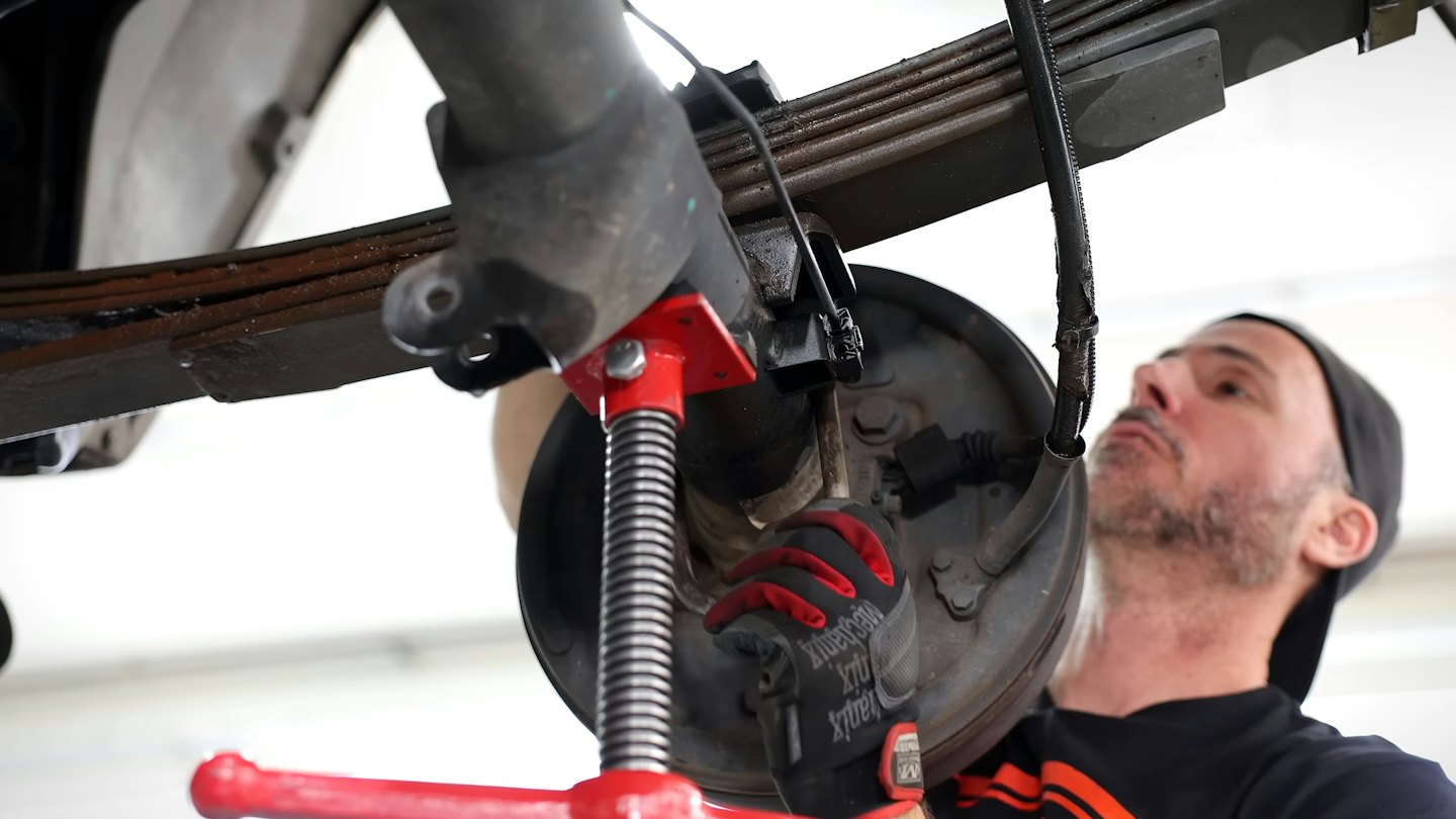 Mechanic working on a vehicle's undercarriage in a garage.